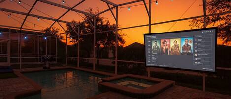 Ein Poolbereich mit transparenter Dachkonstruktion, einer Leinwand, auf der ein Film läuft, und freiem Blick auf den Abendhimmel.