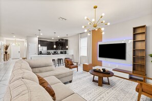 A modern living room with a sectional sofa, a coffee table, and a TV mounted on the wall. - Themed 9BR Villa Pool Game Room Champions Gate (Davenport)