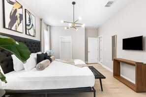 A modern bedroom with a bed, artwork, a television, and a console table. - Themed 9BR Villa Pool Game Room Champions Gate (Davenport)