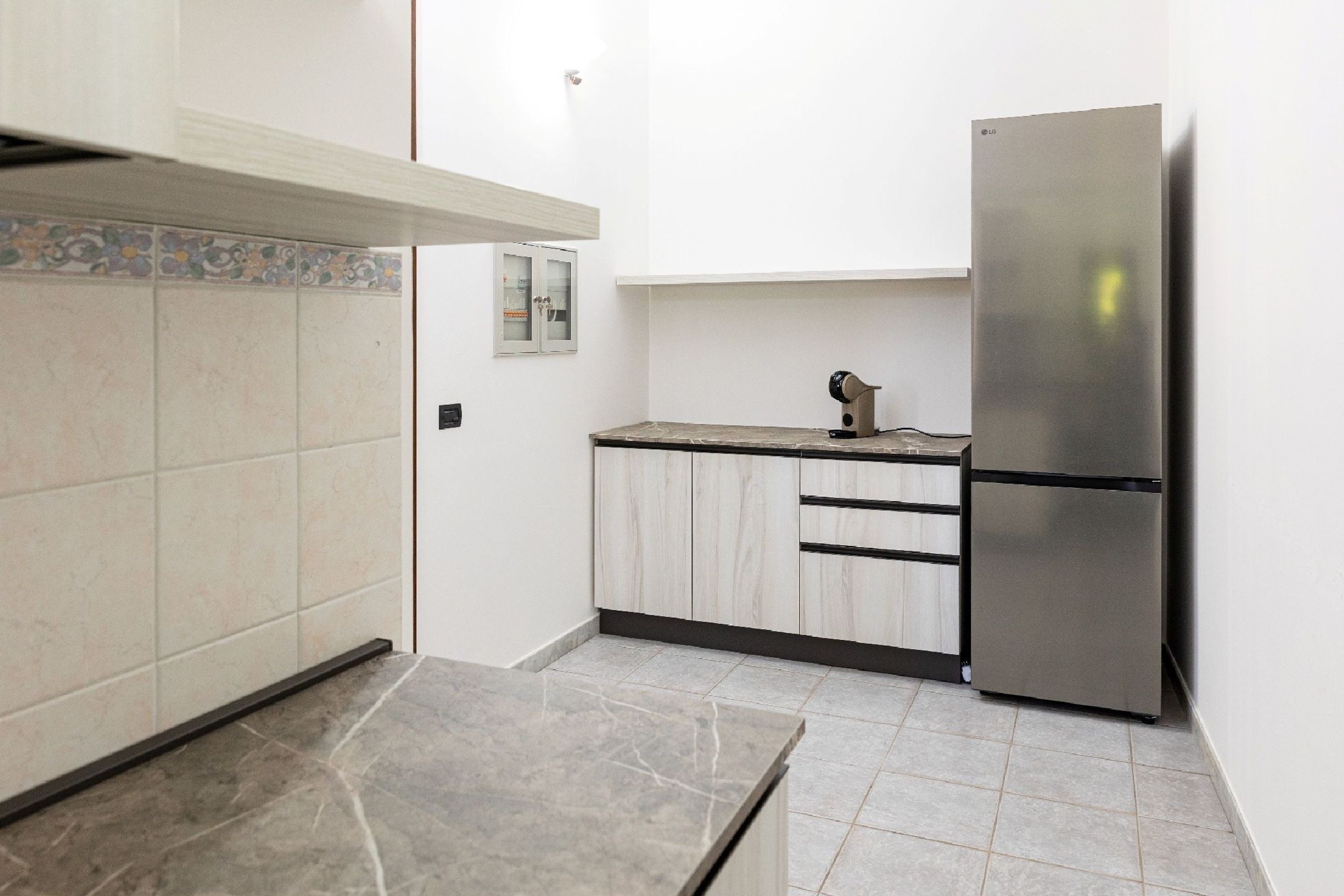 Una cocina con armarios blancos, un refrigerador de acero inoxidable y un salpicadero de azulejos.