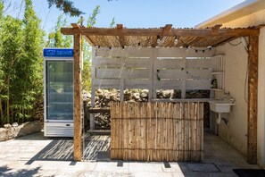 A rustic outdoor bar area with a bamboo fence, a glass-fronted beverage dispenser, and a stone wall backdrop. - Casina Le Rene Con Ampio Giardino e Piscina Privata (Poggiardo)