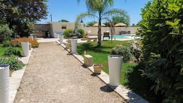 Un sendero de grava que conduce a una zona de piscina con sillones y sombrillas.