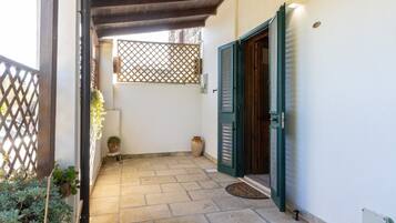Un pequeño patio con piso de baldosas, una pérgola de madera, una puerta verde y plantas en macetas.
