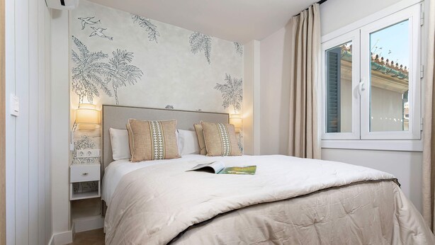 A bedroom with a bed, two bedside lamps, a nightstand, and a window with shutters. - Genteel Home Plaza San Francisco Malaga (Málaga)