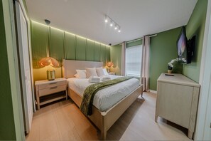 Ein modernes Schlafzimmer mit Bett, Nachttischen, einem Schminktisch und einem an der Wand montierten Fernseher.