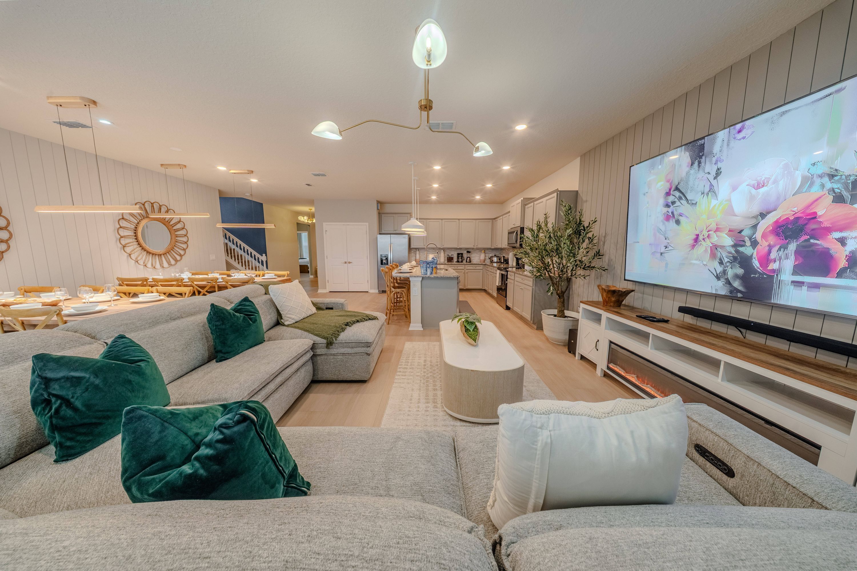 A modern living room with a sectional sofa, a flat-screen TV, and a kitchen in the background.