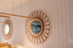 Ein Zimmer mit einem an der Wand befestigten Spiegel mit einem Sonnendesign, einem Holztisch mit Stühlen und einem gerahmten Bild.