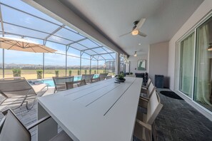 Eine überdachte Terrasse mit einem langen Tisch, Stühlen und Blick auf einen Pool sowie entfernte Gebäude.