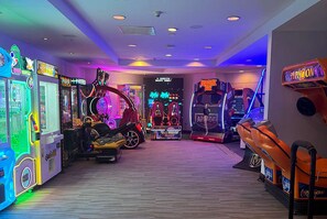 Um salão de jogos indoor com diversas máquinas de entretenimento, incluindo uma atração temática de 'Jurassic Park'.