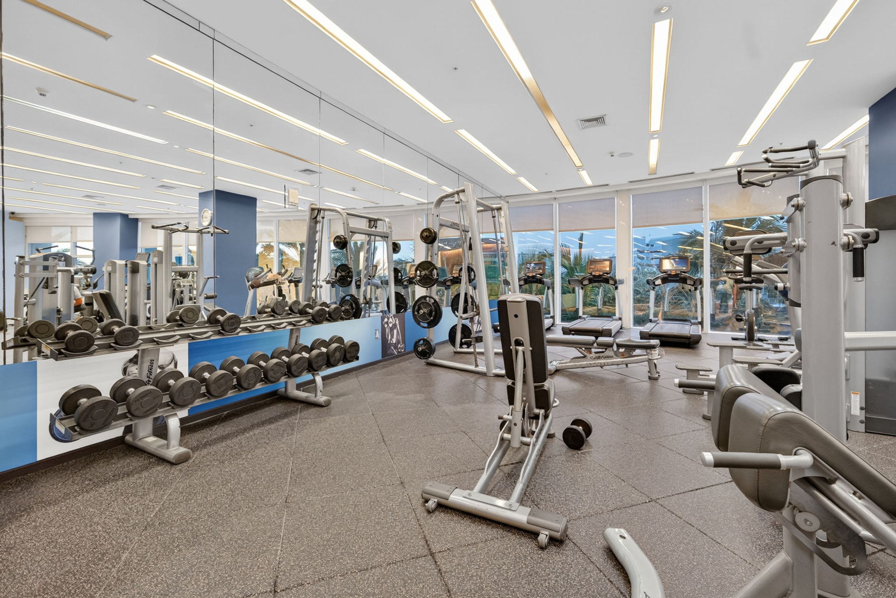 A gym with various exercise equipment, mirrors, and a view of the outdoors.