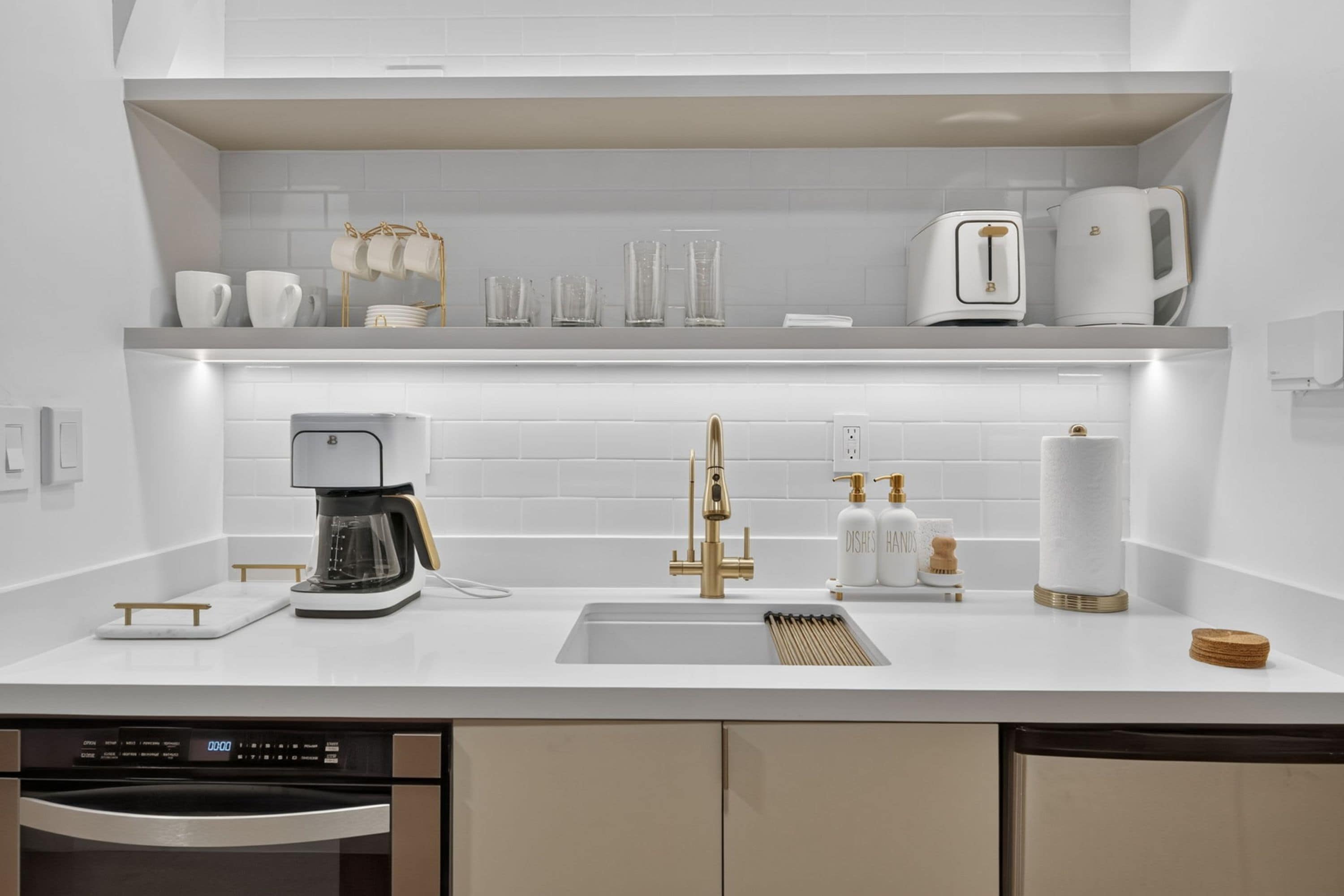 Eine moderne Küche mit eingebautem Geschirrspüler, einer Kaffeemaschine, einem Waschbecken mit Goldarmatur und einer Arbeitsplatte mit verschiedenen Küchenutensilien.