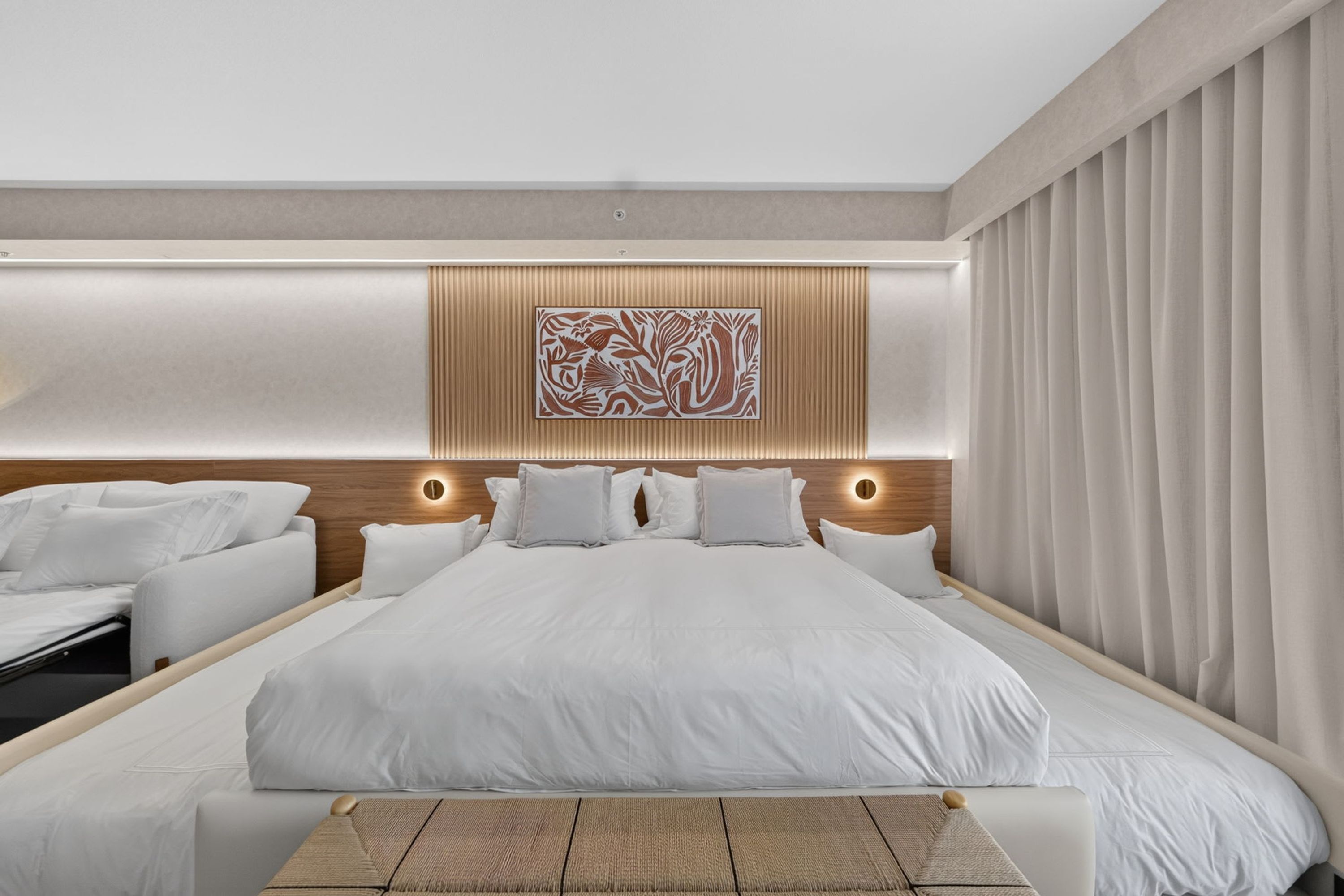 A modern hotel room with a large bed, a seating area, and a decorative wall piece.
