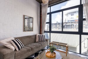 Ein modernes Wohnzimmer mit einer Couch, einem gerahmten Bild und einem großen Fenster mit Blick auf Gebäude.