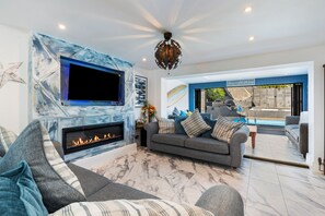 A modern living room with a fireplace, a large flat-screen TV, and a sofa. - Vitamin Sea - Swimming Pool Hot Tub Sea Views (Saundersfoot)