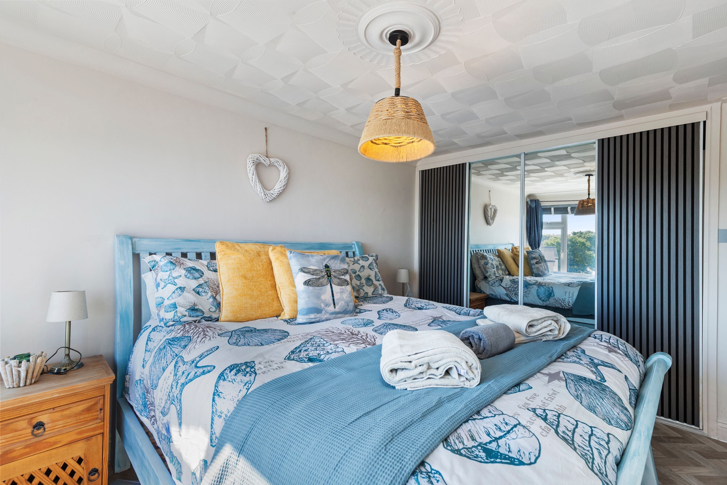 A bedroom with a bed, bedside table, lamp, and a view of the outdoors.