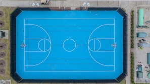 An aerial view of a blue basketball court with two hoops, surrounded by a fence and some greenery. - Go 24 - Windsor Island (Davenport)