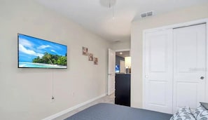A bedroom with a bed, a television mounted on the wall, and a door leading to a bathroom. - Go 24 - Windsor Island (Davenport)