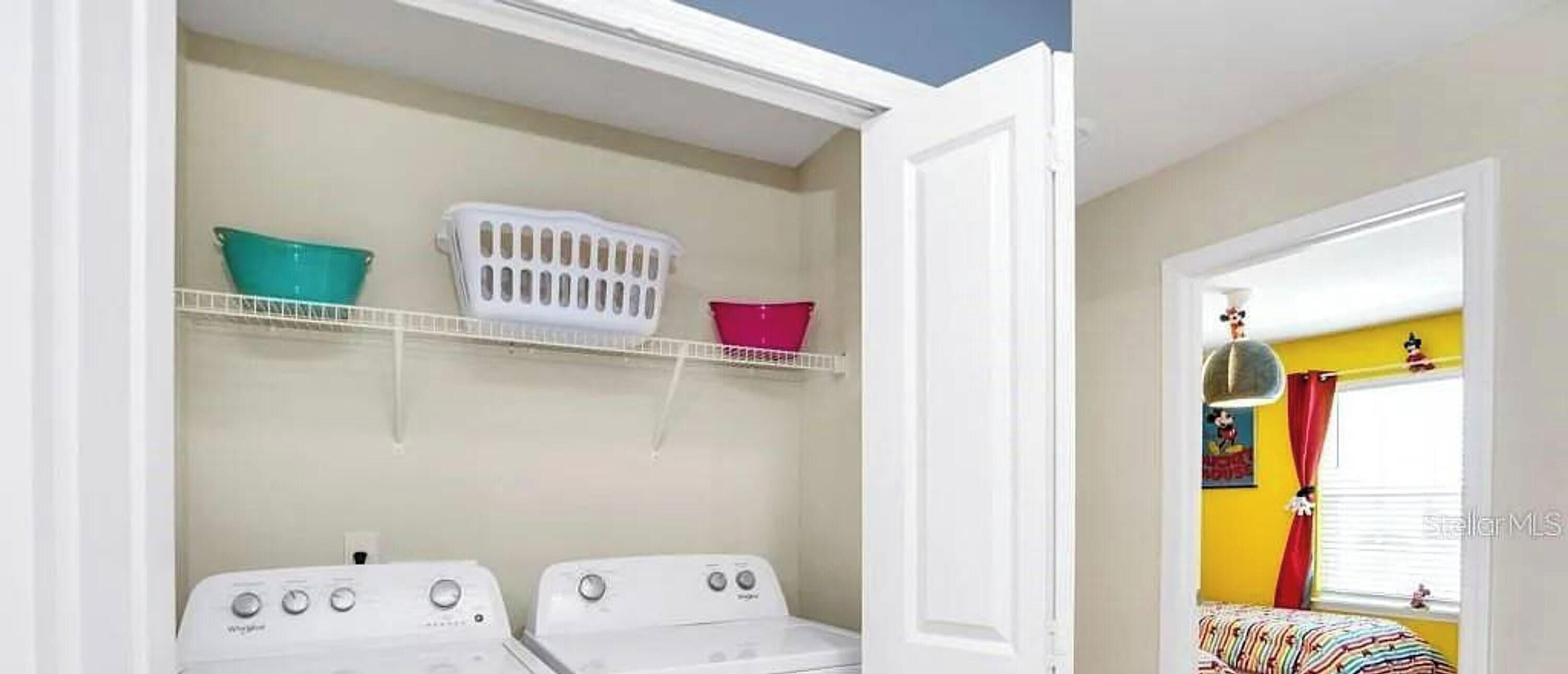 Une buanderie équipée de deux machines à laver, d’un panier à linge blanc et d’un panier rouge posé sur une étagère.