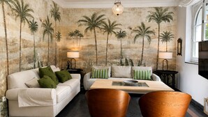 Un salon comprenant un canapé, deux fauteuils, une table basse et une fresque murale représentant des palmiers.