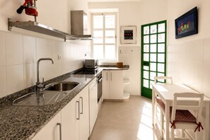 A kitchen with white cabinets, a granite countertop, a sink, a microwave, and a green-framed door. - Genteel Home Bartolom de Medina (Seville)