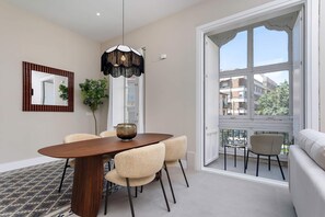 A dining area with a wooden table, woven chairs, a hanging light fixture, and a view through a large window. - Genteel Home San Anton 104 (Granada)