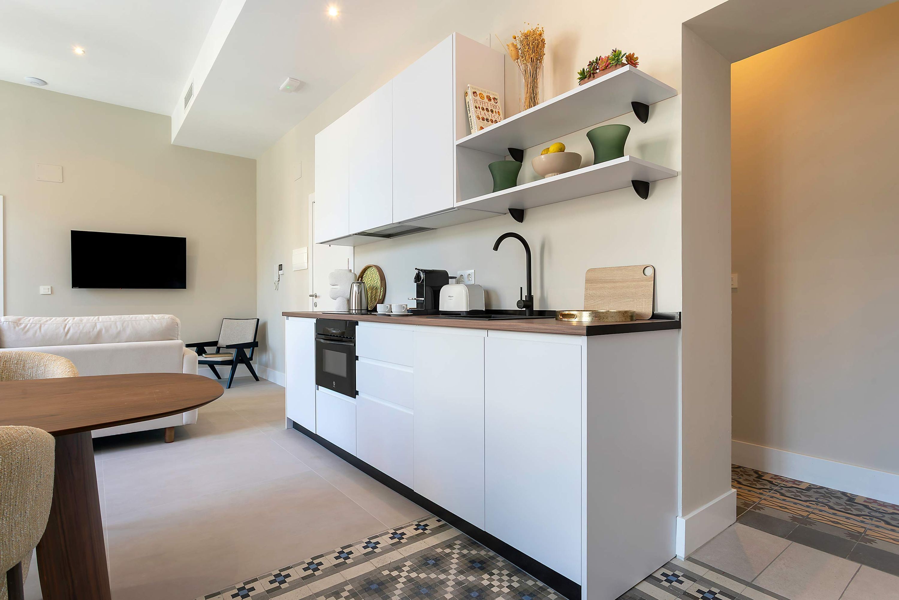 A modern kitchen with white cabinetry, a built-in oven, and a coffee machine.