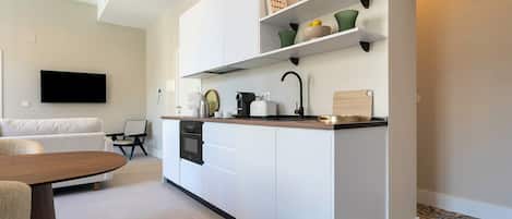 A modern kitchen with white cabinetry, a built-in oven, and a coffee machine.