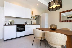 Eine moderne Küche mit weißen Schränken, einem Einbauofen und einem Essbereich mit Holztisch und gewobenen Stühlen.