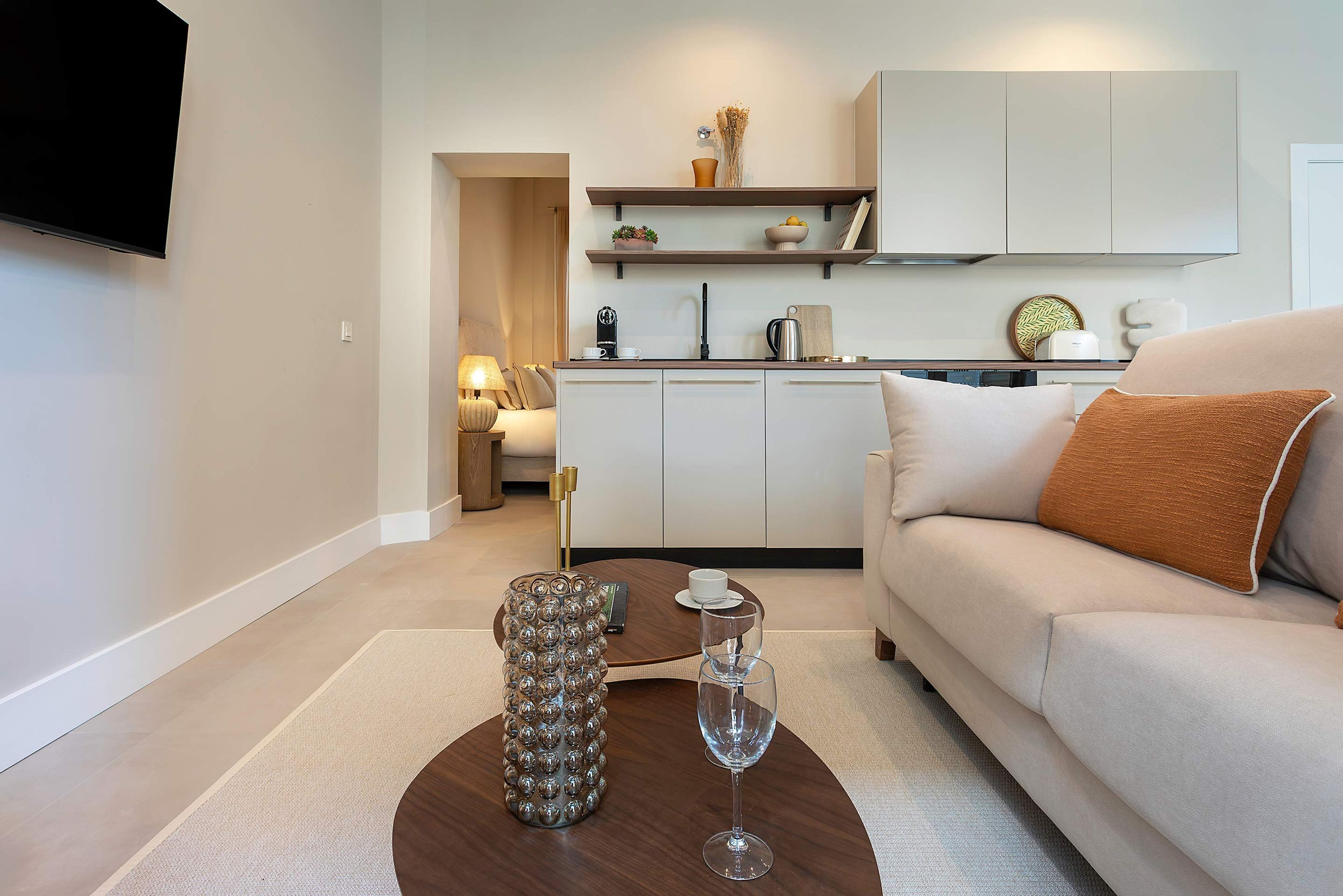 Una sala moderna con un sofá, una mesa de centro con objetos decorativos y una cocina al fondo.