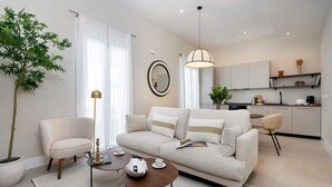 Una sala moderna con un sofá, sillones, una mesa de centro y un comedor con una cocina al fondo.