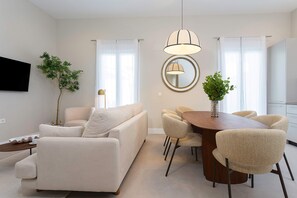 A modern living room with a sofa, dining table, chairs, and a TV mounted on the wall. - Genteel Home San Anton 102 (Granada)