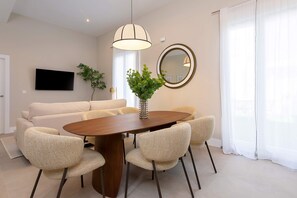 A modern dining area with a round wooden table, six upholstered chairs, a large mirror, and a flat-screen TV mounted on the wall. - Genteel Home San Anton 102 (Granada)