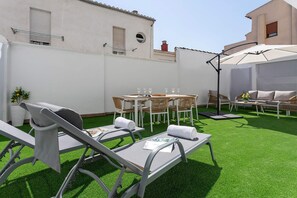 Eine Dachterrasse mit Kunstrasen, Gartenmöbeln und einer Pergola, die Schatten spendet.
