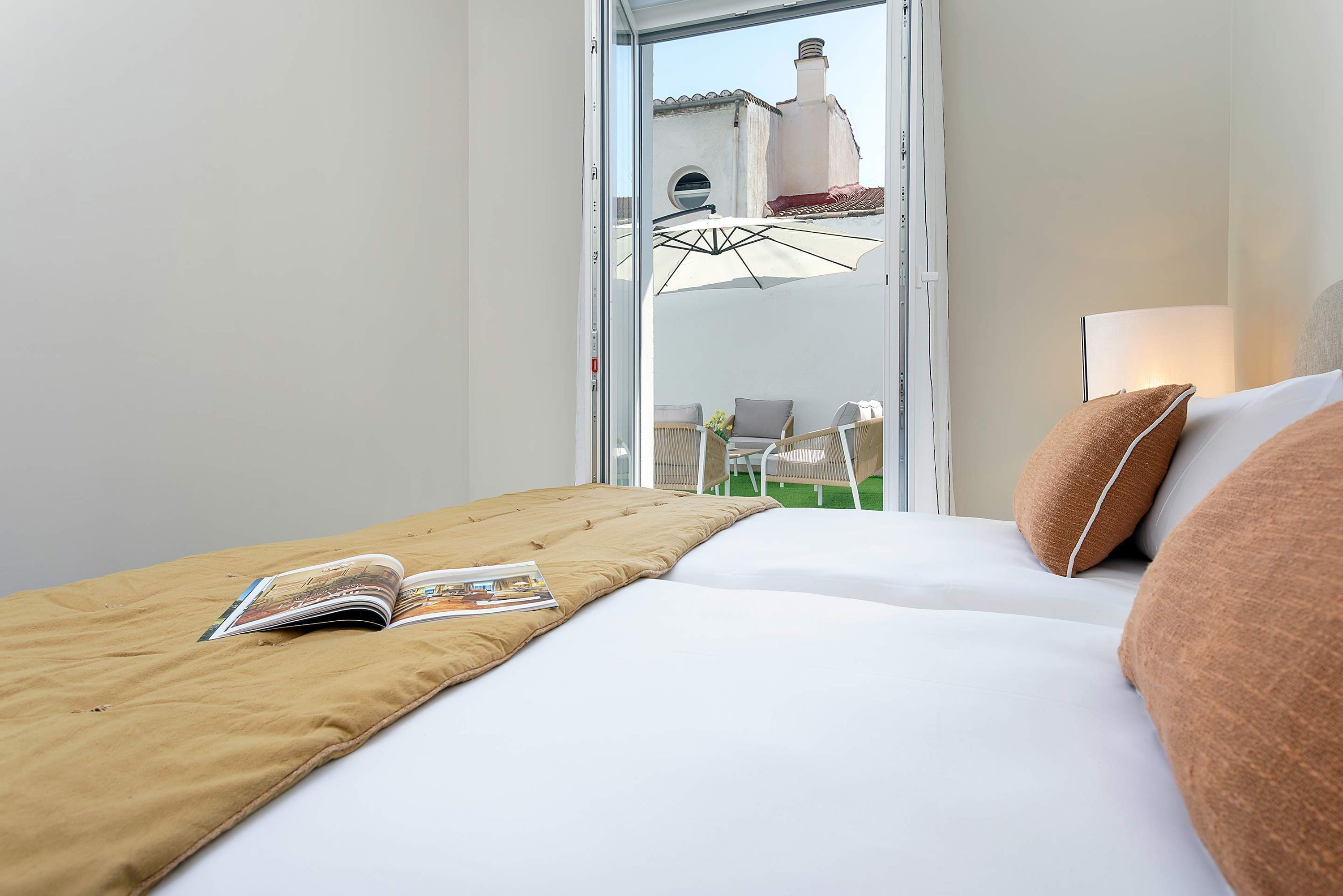 A hotel room with a bed, a window, a magazine on the bed, and a view of the outside.