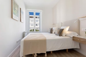 A bedroom with a bed, bedside tables, a nightstand, a lamp, and a view of a building through a window. - Genteel Home Reina Sof a IV (Madrid)