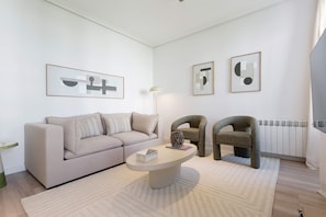 A modern living room with a sofa, two armchairs, a coffee table, and abstract wall art. - Genteel Home Reina Sof a IV (Madrid)