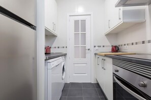 A compact kitchen with a washing machine, a red kettle, and a stove. - Genteel Home Reina Sof a IV (Madrid)