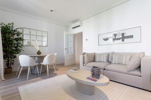 A modern living room with a white sofa, a round coffee table, and a dining area with two chairs and a small table. - Genteel Home Reina Sof a IV (Madrid)