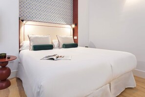 A neatly made bed with white bedding and two pillows, a bedside table with a remote control and a candle, and a patterned wall above the bed. - Genteel Home Padre Marchena 13 002 (Seville)