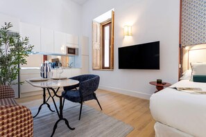 A compact hotel room with a kitchenette, a dining area, a TV mounted on the wall, and a bed with a bedside table. - Genteel Home Padre Marchena 13 002 (Seville)