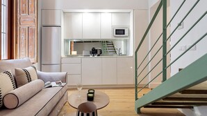 Eine moderne Küche mit weißen Schränken, einer Mikrowelle und einem Toaster. Eine Holztreppe mit grüner Geländer führt zu einer oberen Ebene.