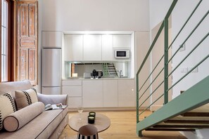 Eine moderne Küche mit weißen Schränken, einer Mikrowelle und einem Toaster. Eine Holztreppe mit grüner Geländer führt zu einer oberen Ebene.