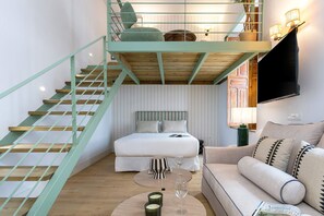 Ein kompakter Wohnraum mit Schlafgalerie, einer Treppe, einer Couch und einem Flachbildfernseher.