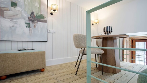Ein Zimmer mit Holzboden, einem runden Holztisch mit einer gestreiften Tasse, einer gepolsterten Bank und einer wandmontierten Leuchte.