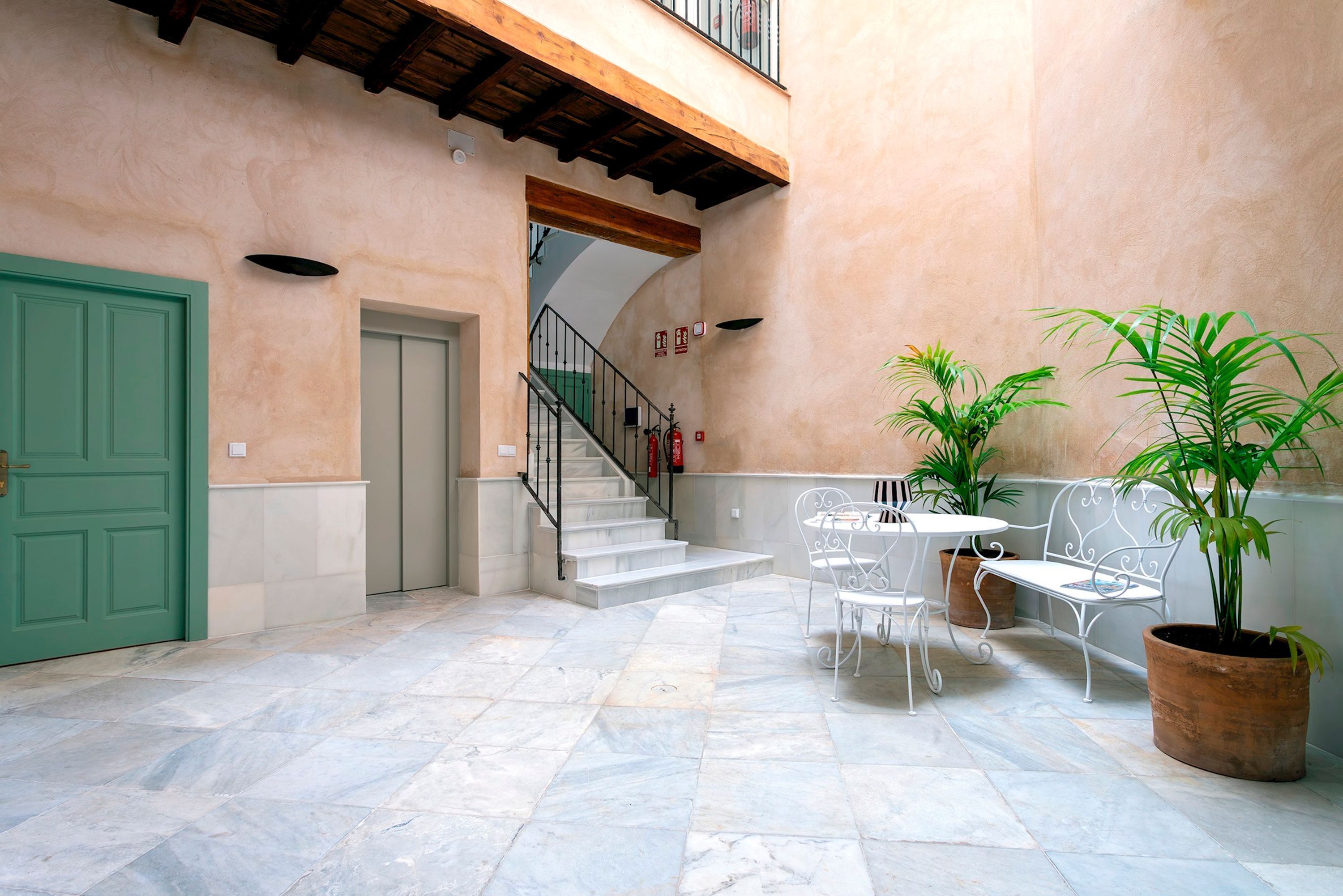 Un patio con una puerta verde, una escalera y mobiliario exterior con plantas en macetas.