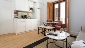 Un espacio habitable compacto con kitchenette, un área de comedor con mesa y sillas, y vista a través de una puerta abierta.
