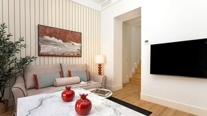 Una sala de estar moderna con un sofá, un televisor de pantalla plana montado en la pared, una mesa de centro de mármol con jarrones decorativos y una planta en maceta.