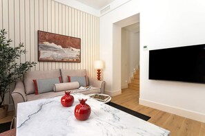 Ein modernes Wohnzimmer mit einer Couch, einem an der Wand befestigten Flachbildfernseher, einem Marmortisch mit dekorativen Vasen und einer Topfpflanze.