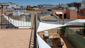Eine Dachterrasse mit Blick auf die Stadtlandschaft, mit einem weißen Sonnenschirm, einem Stuhl und einem Tisch.