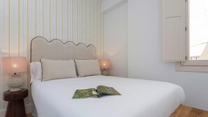 Ein ordentlich bezogenes Bett mit einem Buch darauf, einer Nachttischlampe und einer gestreiften Wand.